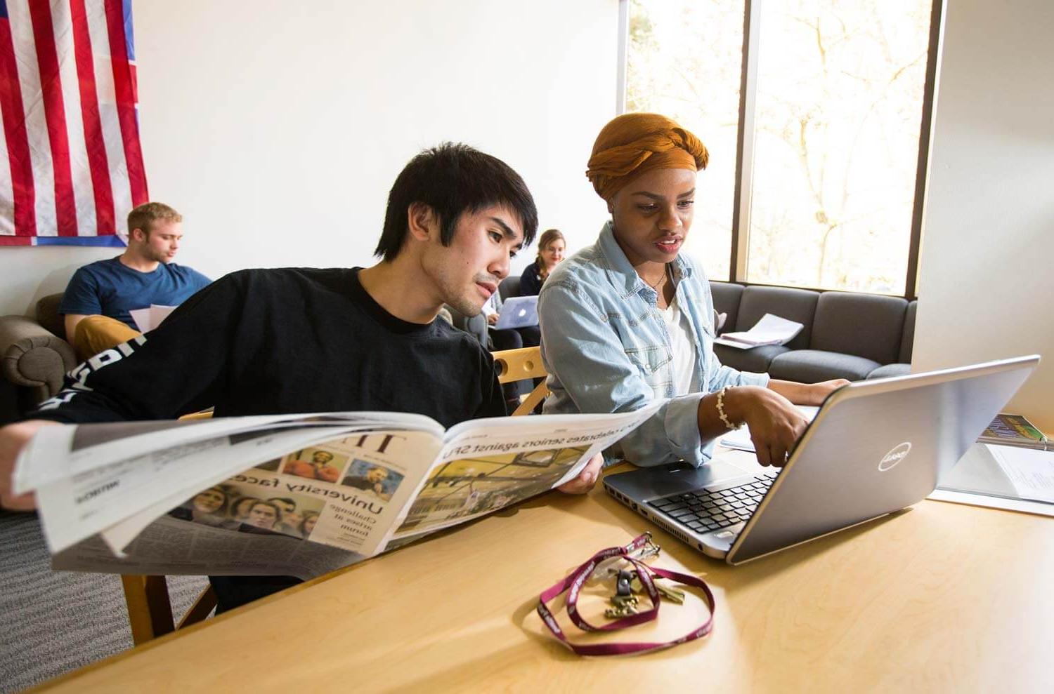 Students looking at laptop and newspaper